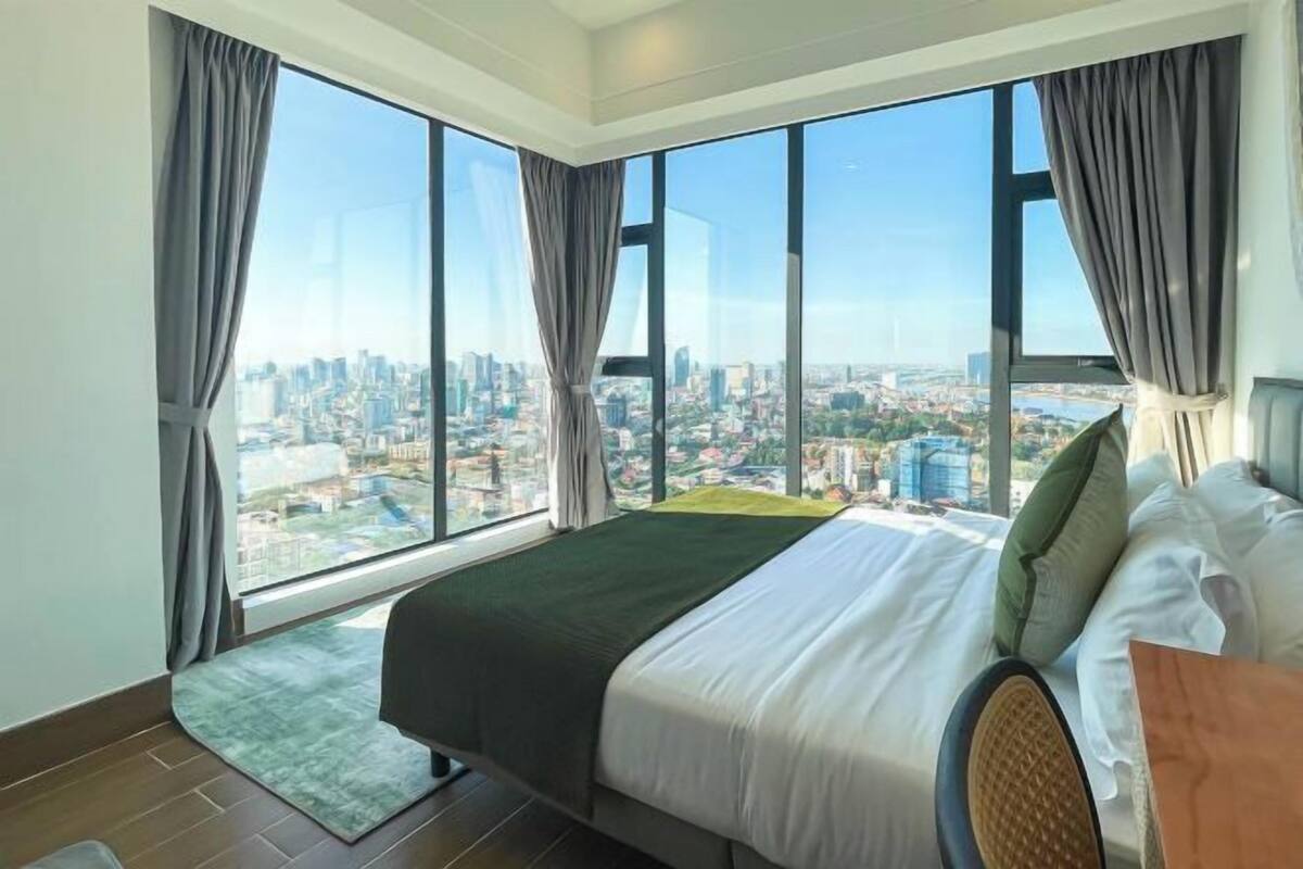 Une chambre d’hôtel moderne, dotée d’un grand lit, offrant une vue sur le paysage urbain et une vue sur la ville à travers de grandes fenêtres.