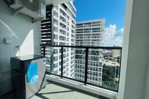 Ein Balkon mit Blick auf ein Hochhaus, ein kleiner Tisch mit einem blauen Gegenstand und eine Klimaanlage.