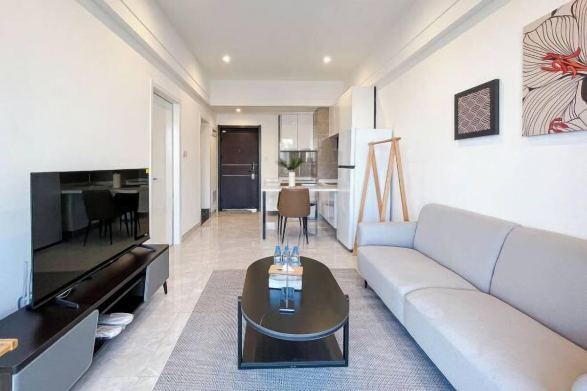 Un salon moderne avec un téléviseur à écran plat, un canapé, une table basse et un coin repas à l’arrière-plan.