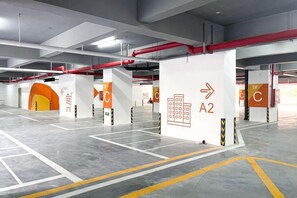 Un parking intérieur doté d’une signalisation claire indiquant les directions, de places de stationnement délimitées et de piliers de soutien.