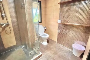 A bathroom with a glass-enclosed shower, a toilet, and a trash bin.