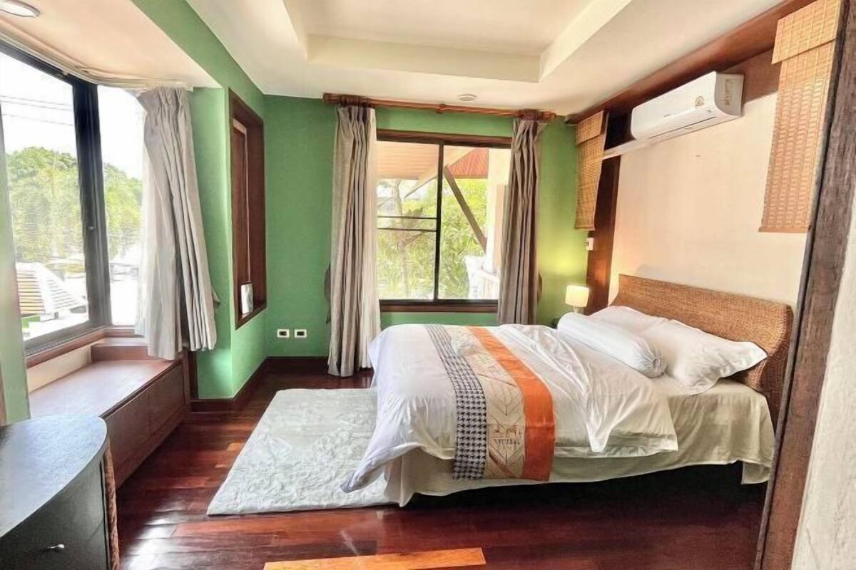 A bedroom with a bed, a window, a bench, and an air conditioning unit.