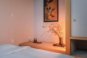 Un dormitorio con una cama, una mesita de noche con un jarrón de flores secas y un cuadro en la pared.