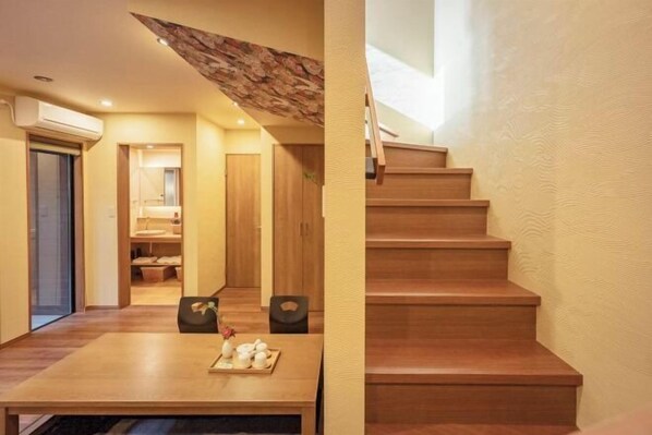 Una escalera de madera que conduce a un piso superior, una mesa de comedor de madera con una bandeja de teteras y un pasillo con una puerta de madera y un espejo.