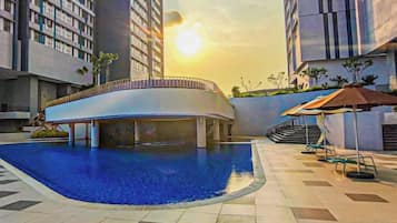 A swimming pool surrounded by modern buildings, with a sun setting in the background.