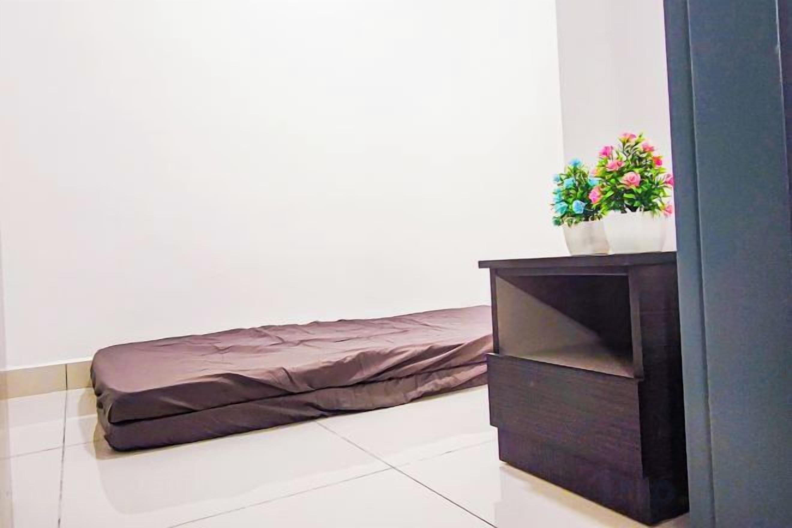 A room with a mattress against a wall, a dark-colored cabinet with a potted plant on top, and a tiled floor.
