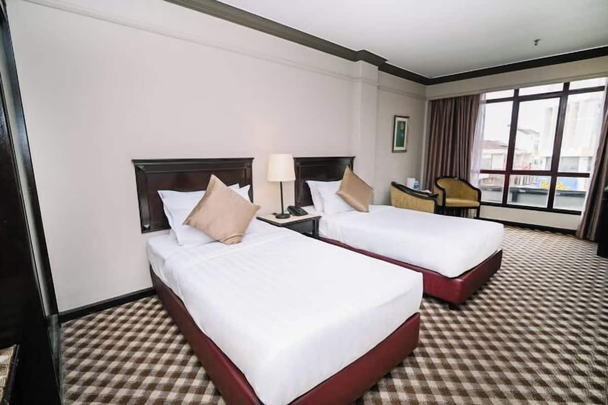 Una camera d'albergo con due letti, una scrivania, una sedia e un'ampia finestra.