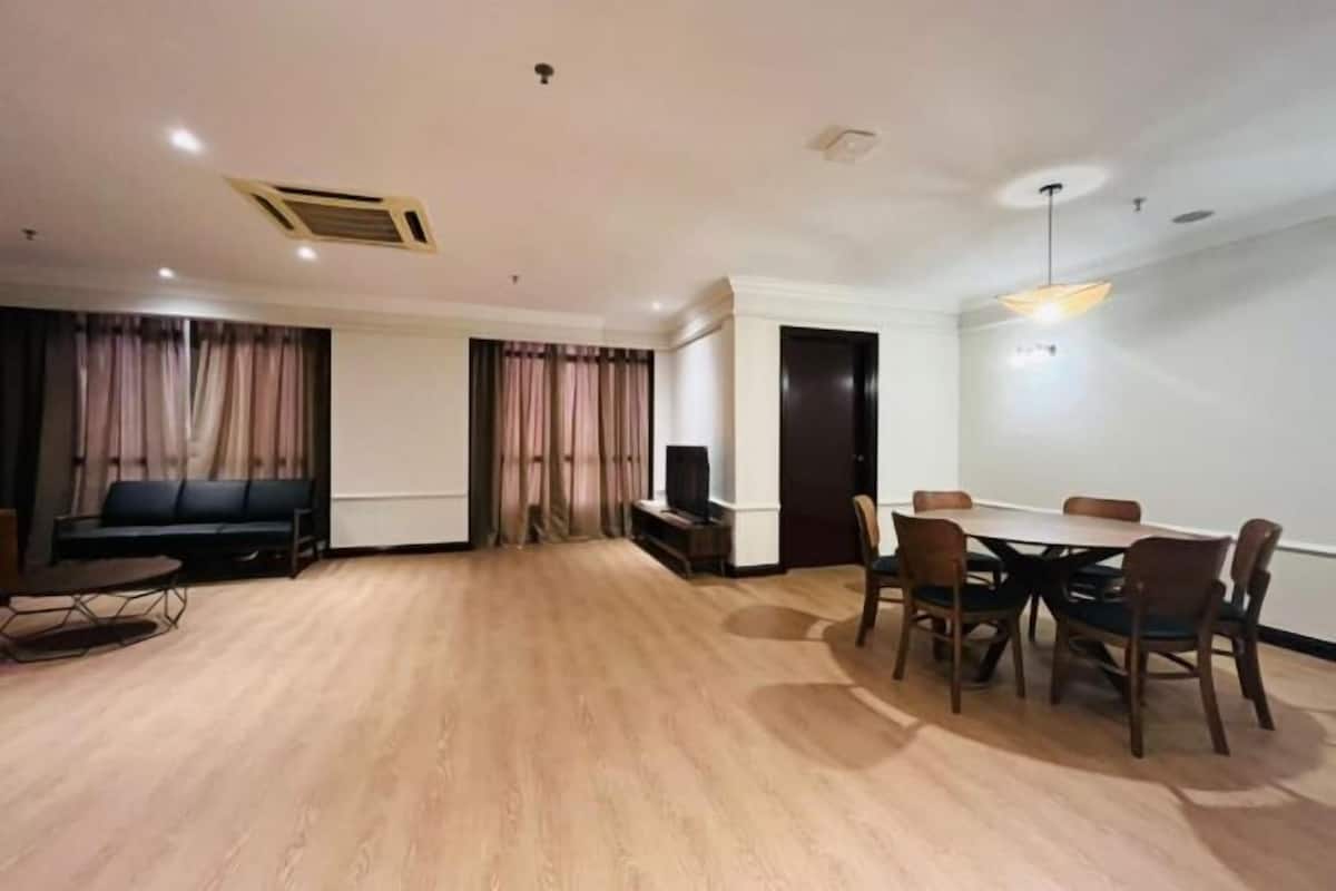Un soggiorno moderno con zona pranzo, pavimento in legno, un divano, una TV e un lampadario.