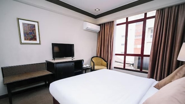 Ein Hotelzimmer mit einem großen Bett, einem Schreibtisch mit Fernseher, einem Sessel und einem Fenster mit Vorhängen.