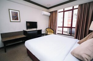 Una habitación de hotel con una cama grande, un escritorio con televisor, una silla y una ventana con cortinas.
