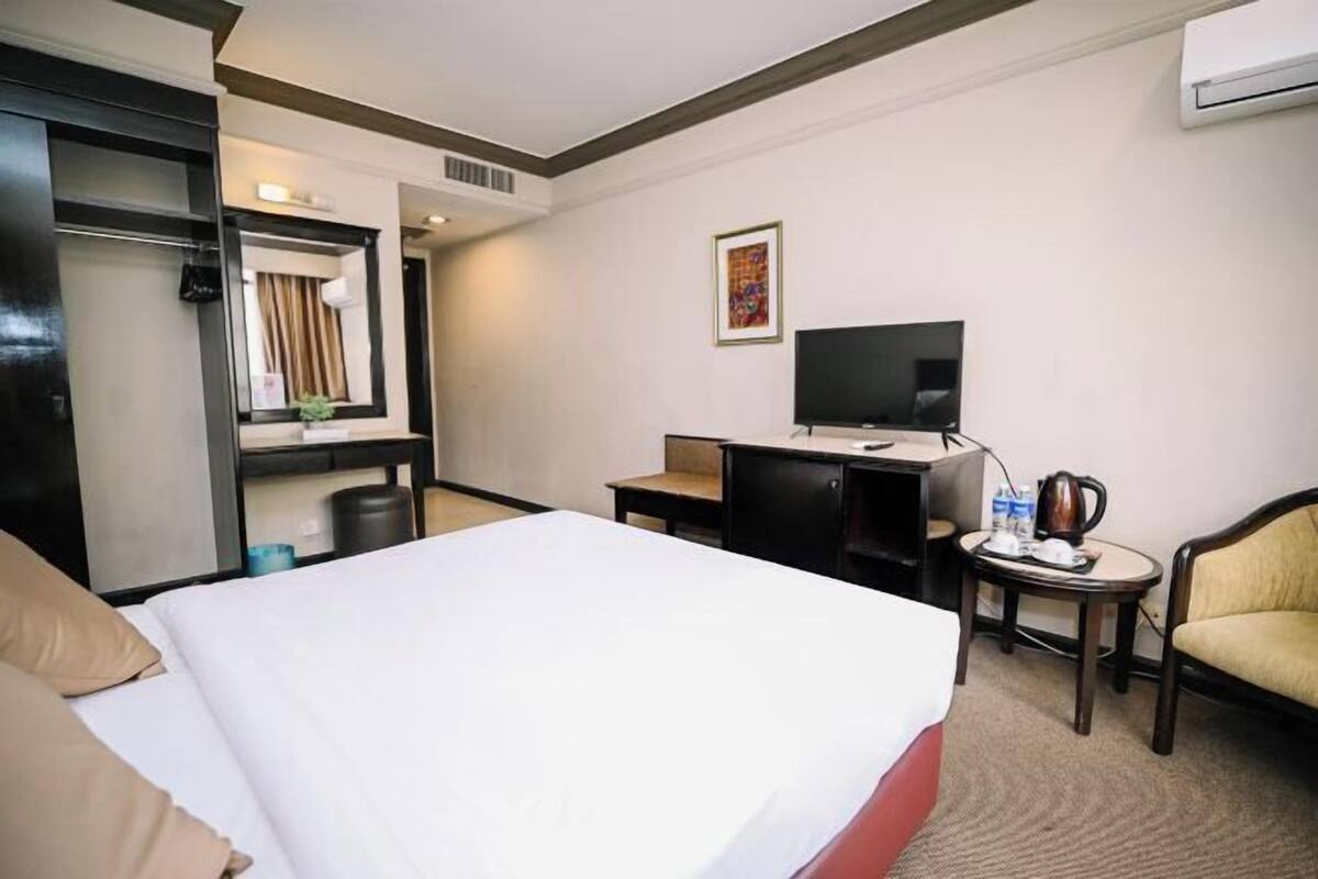 Una camera d'albergo con un letto, una scrivania, una sedia, un televisore e un tavolino con un bollitore.