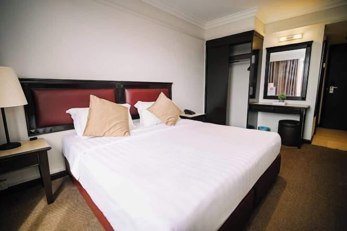 Una camera d'albergo con un letto grande, un comodino con una lampada, una piccola scrivania con uno specchio e un cestino.