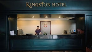 Ein Empfangsbereich im Kingston Hotel mit einer Rezeptionistin, einer Blumendekoration und einem Schild über dem Schreibtisch.
