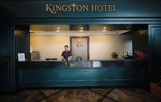 Un mostrador de recepción en el Hotel Kingston, con una recepcionista, una decoración floral y un cartel sobre el mostrador.
