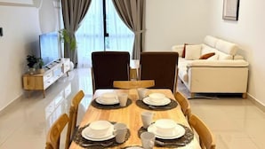 Un salon moderne avec une table à manger pour quatre personnes, un canapé, un téléviseur et une grande fenêtre avec des rideaux.