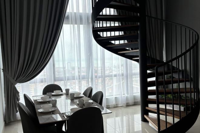 Un comedor con una mesa dispuesta para cuatro, una escalera de caracol y un gran ventanal con cortinas translúcidas.