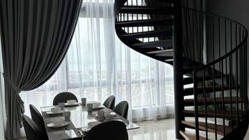 Un comedor con una mesa dispuesta para cuatro, una escalera de caracol y un gran ventanal con cortinas translúcidas.