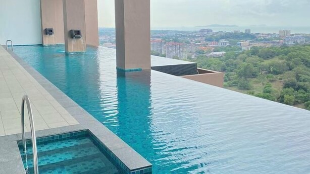 Une piscine à débordement située sur le toit, avec une eau d’un bleu cristallin, entourée de piliers de couleur beige, et offrant une vue panoramique sur la ville, avec ses bâtiments et sa végétation.