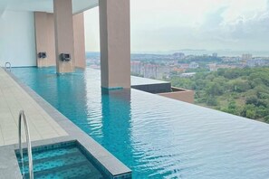 A rooftop infinity pool with clear blue water, surrounded by beige pillars, overlooking a cityscape with buildings and greenery. - The Apple Melaka by Iconique (Melaka)