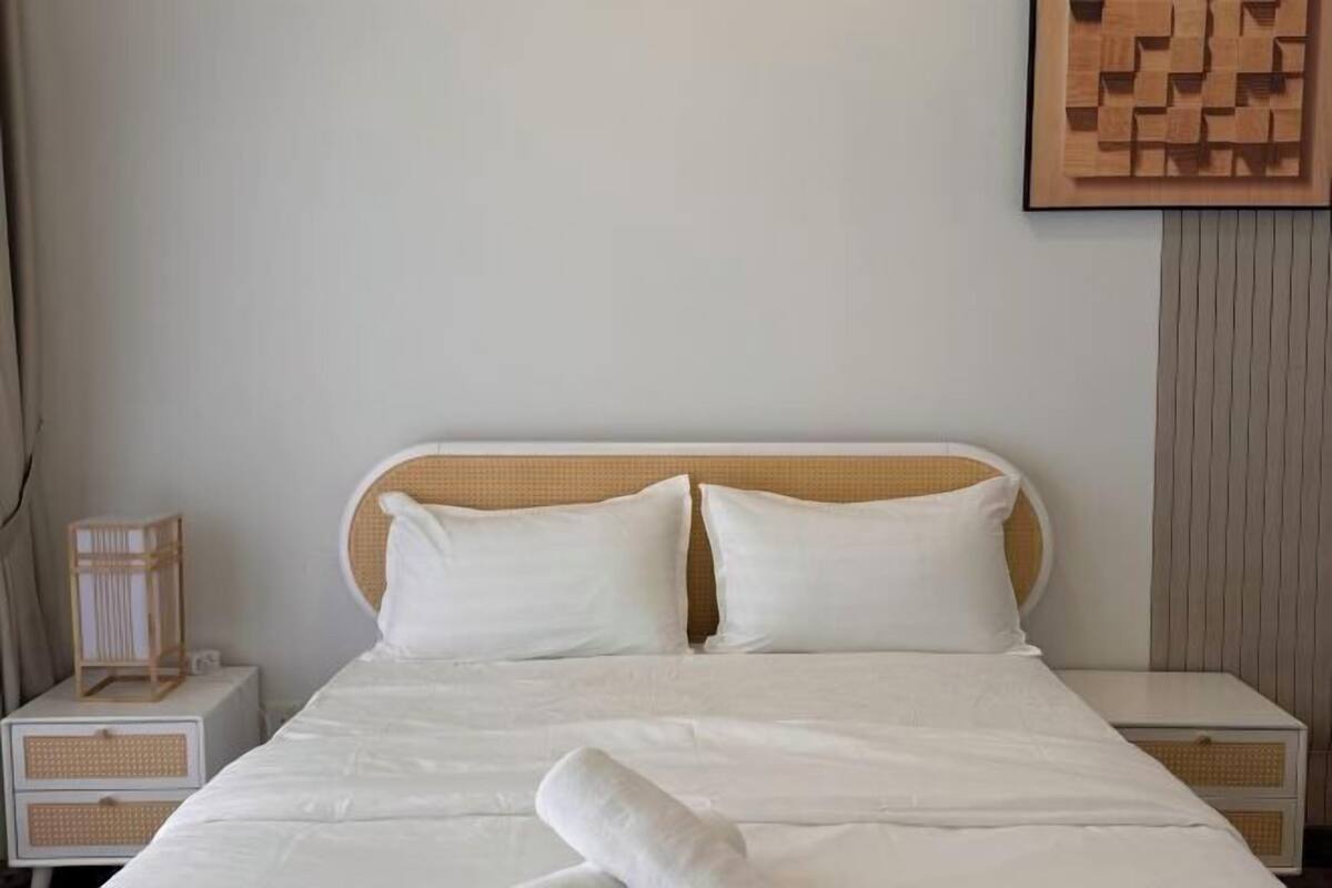 Ein ordentlich gemachtes Bett mit weißer Bettwäsche, zwei Kissen und einem hölzernen Kopfteil. An jeder Seite des Bettes stehen Nachttische mit gewebten Körben.