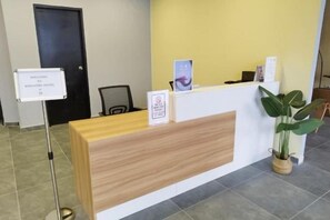 A reception desk with a sign, a plant, and a door in the background. - Kingston Hotel 7 @ Johor Bharu (Johor Bahru)