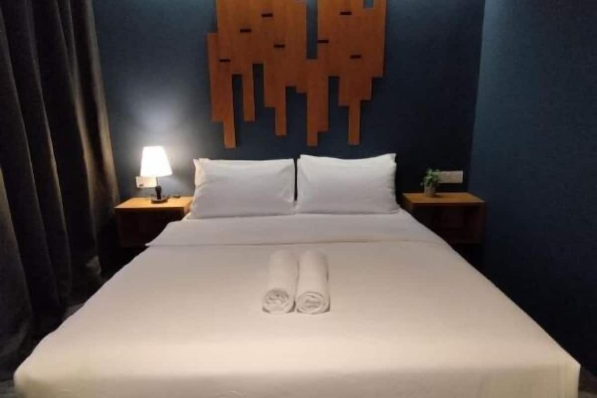 A hotel room with a neatly made bed, a bedside lamp, and a wall-mounted wooden panel.