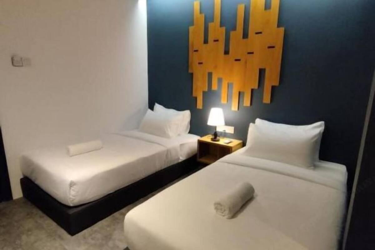 A hotel room with two beds, a wall-mounted light, and a modern abstract wall decoration.