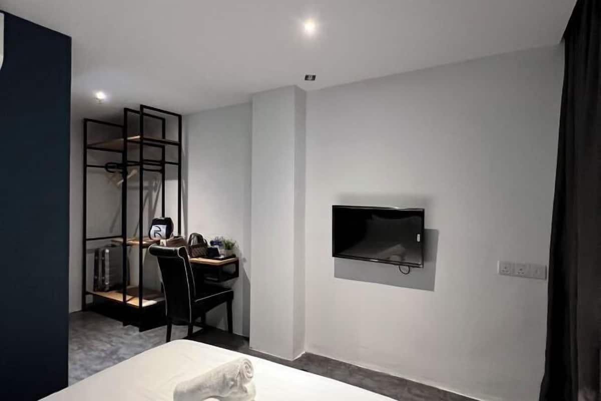 A modern hotel room with a bed, a desk with a chair, a TV mounted on the wall, and a wardrobe with a mirror.
