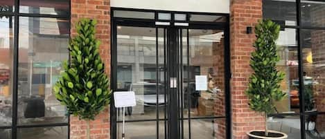 A building entrance with glass doors, two potted plants, and a sign.