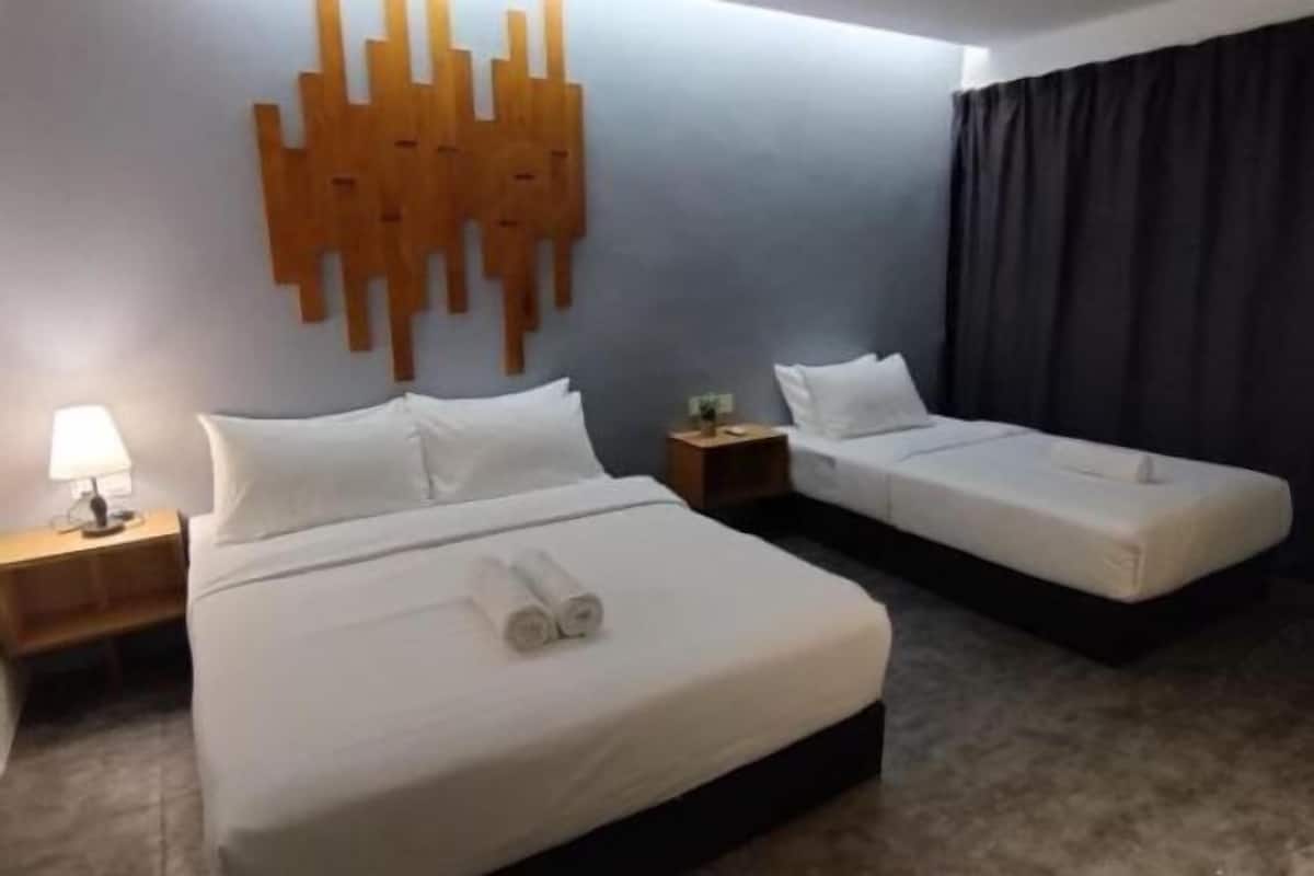 A hotel room with a large bed, two smaller beds, a wooden wall decoration, a nightstand with a lamp, and a dark curtain.
