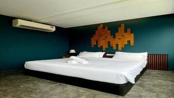 A hotel room with a bed, a wall-mounted air conditioner, and a decorative wall piece.