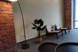 Een kamer met een bakstenen muur, een potplant, twee stoelen en een vloerlamp.