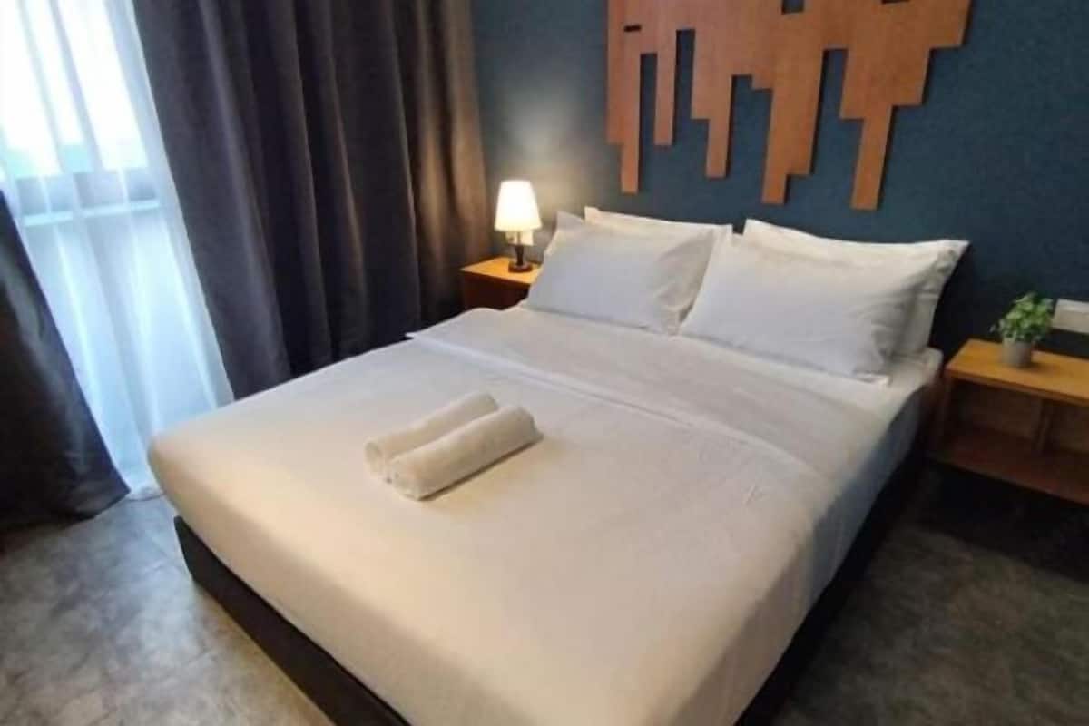 A neatly made bed with white linens and two rolled towels, a bedside lamp, and a wooden wall decor piece.