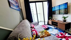 A modern living room with a sofa, a flat-screen TV, a small wooden side table, and a large window with curtains. - VIM3 Desa Park North Desa Parkcity ISP school Damansara Kepong Kuala Lumpur (Kuala Lumpur)