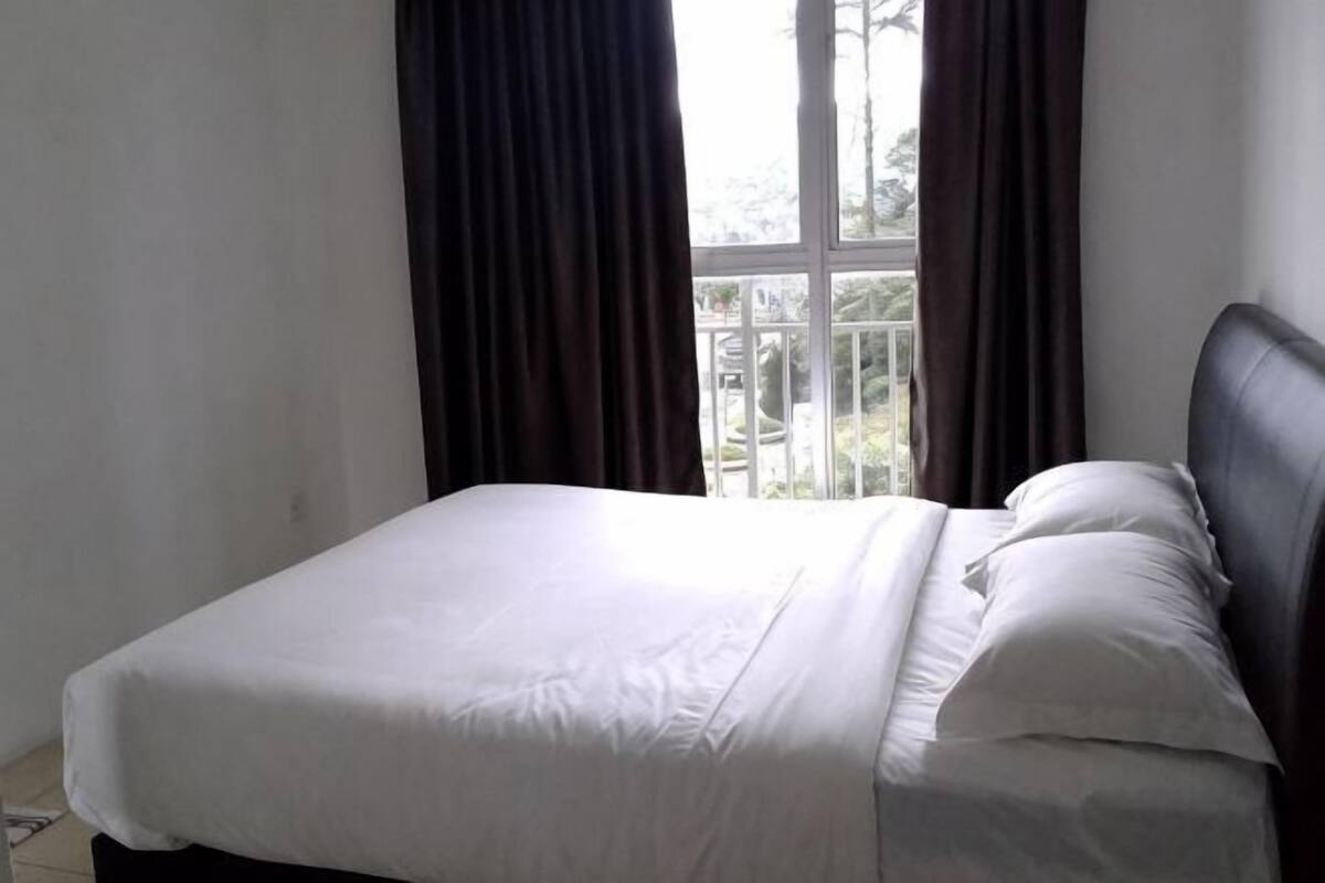 A bed with white linens, a dark headboard, and a window with curtains.