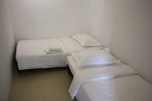 Two single beds with white linens in a small, plain room with a tiled floor.
