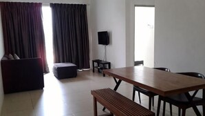 Een kamer met een houten tafel, zwarte stoelen, een rode bank, een klein voetenbankje, een televisie op een dressoir en een raam met gordijnen.
