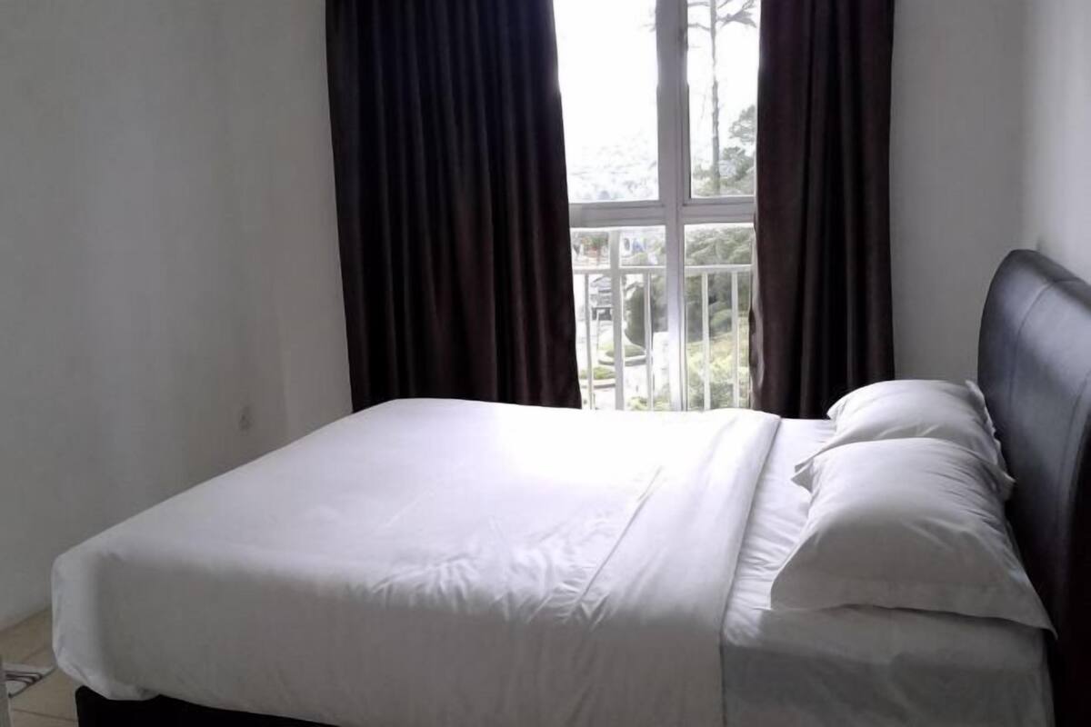 A bed with white bedding, a dark headboard, and a window with curtains.