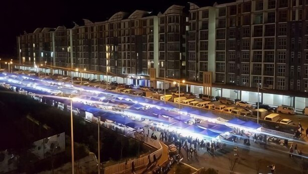 Een meerlaags hotel met een rij balkons, een overdekt buitengebied met verlichting en een parkeerplaats.