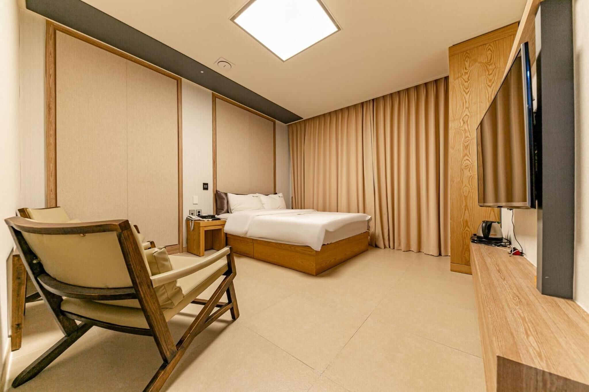 A modern hotel room with a bed, a wooden chair, a desk, and a TV.
