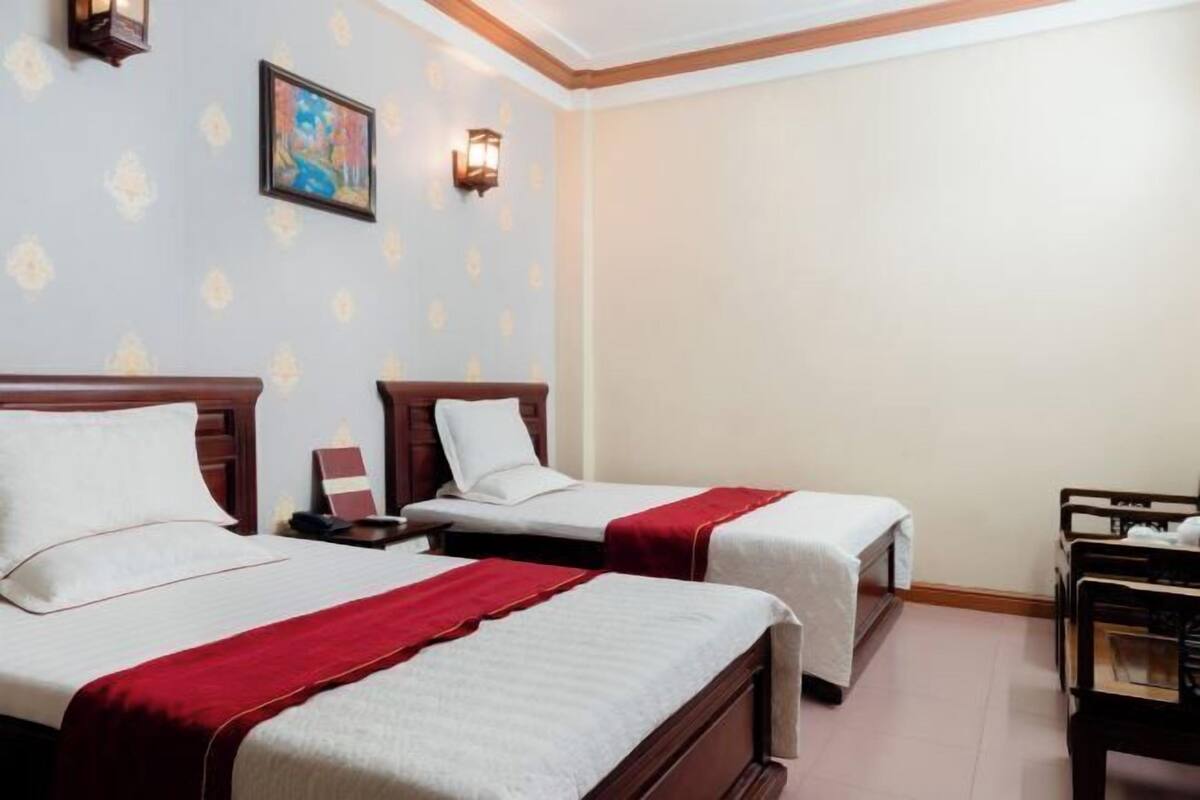 Une chambre d’hôtel avec deux lits, une tête de lit en bois, une table de chevet, un bureau et une chaise.