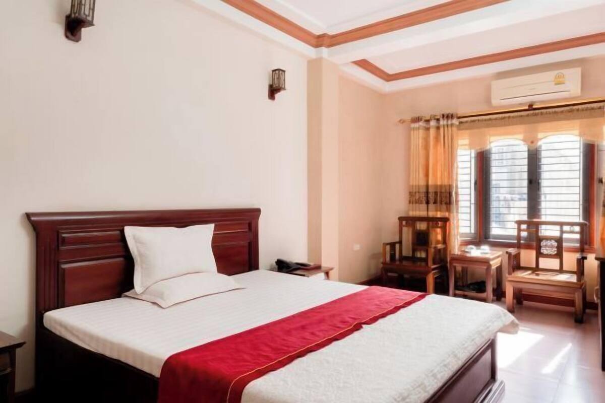 Une chambre d’hôtel avec un lit en bois, un plaid rouge, un bureau et une chaise.