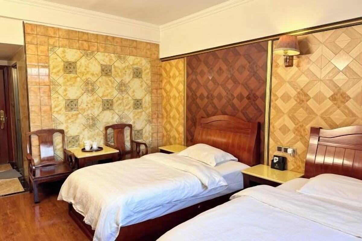 A hotel room with two beds, a wooden headboard, a small table with a lamp, and a chair.