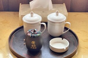 A tray with two white teapots, a teapot with a colorful lid, and a white cup on a wooden table. - SHENGCHANG HOTEL (Muang Xai)