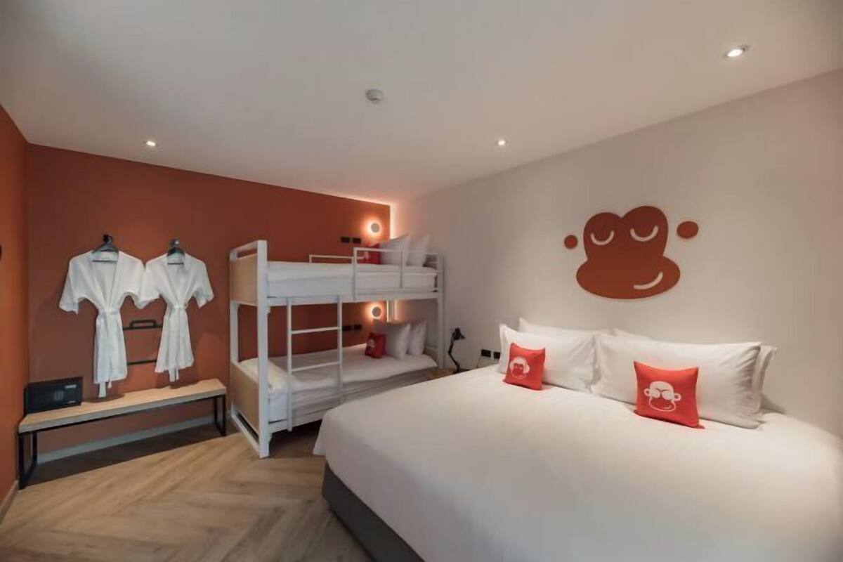 Une chambre d’hôtel avec un lit superposé, un grand lit avec des oreillers et un mur décoré d’un personnage de dessin animé.
