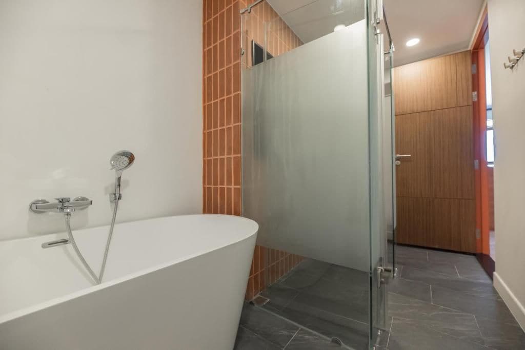 Un baño moderno con una bañera independiente, cabina de ducha con mampara de cristal y puerta de madera.