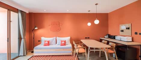 A room with a bed, a desk, and a chair. There is a window with curtains, a wall clock, and a wall-mounted light fixture.