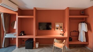 Une pièce avec un téléviseur fixé au mur, un bureau avec une chaise, une petite étagère avec une lampe et un porte-manteau avec un peignoir.