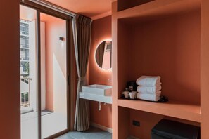 Une salle de bain moderne avec une porte coulissante en verre, un lavabo blanc, un miroir et une étagère avec des serviettes et des tasses.