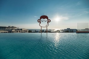A pool with a large cartoon monkey figure in the center, surrounded by buildings and palm trees. - BLU Monkey Hub & Hotel Bangsaen (Chonburi)